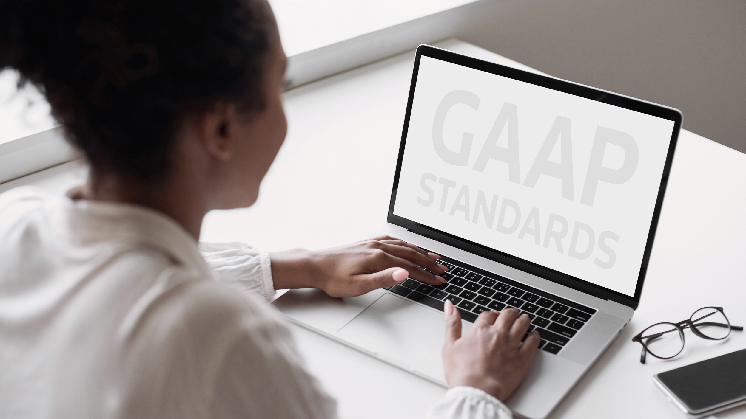 A Black female accountant looks at a laptop screen that has the words 'GAAP standards' against a white screen.