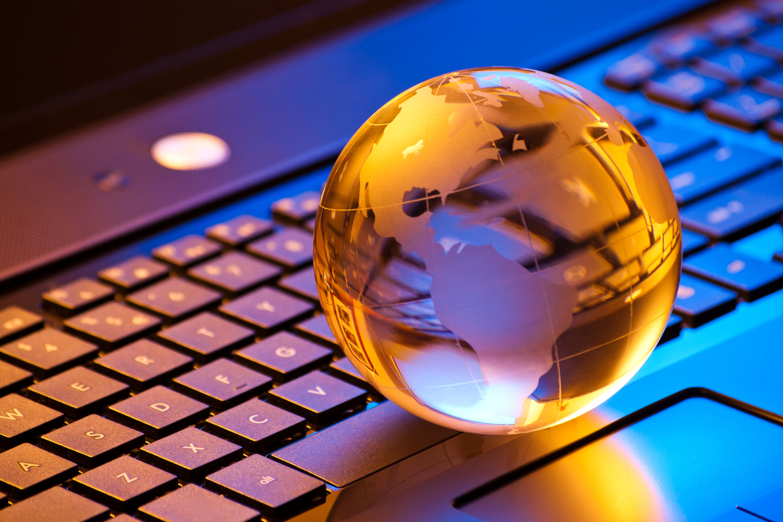 Closeup of a small metal globe sitting on a keyboard reflecting yellow, blue, and purple light.