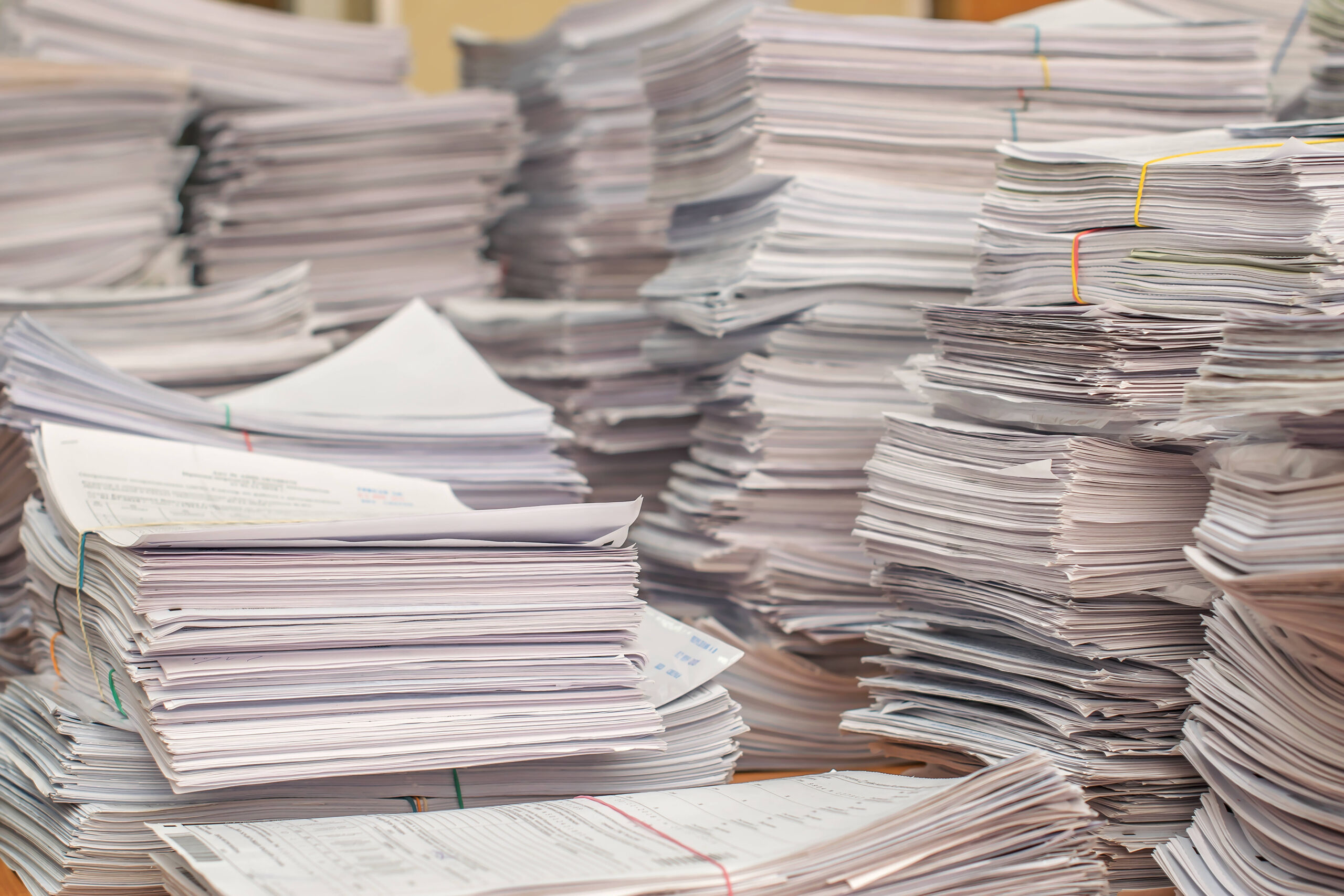 Several high stacks of paper documents on an office desk.